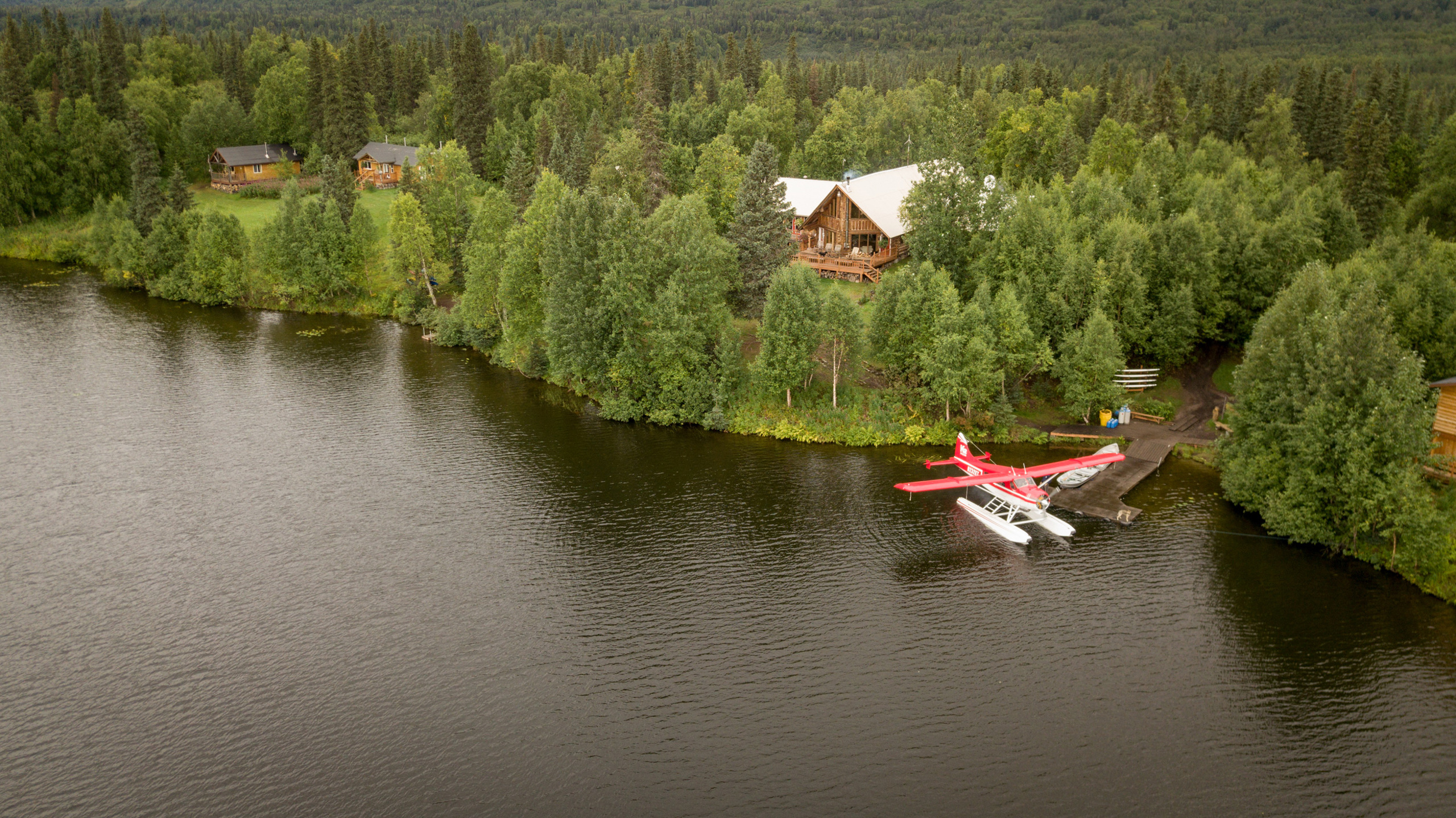 Exterior of a log cabin, Eleven Winterlake Lodge, surrounded by trees with a lake in front.